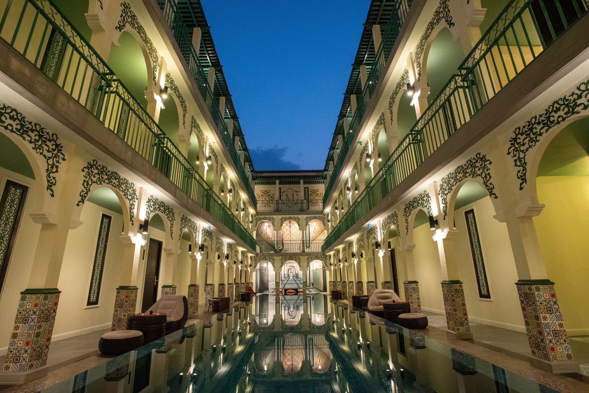 Eleganter Hotelinnenhof im marokkanischen Stil mit Pool und kunstvollen Bögen, eingefangen in der Dämmerung.