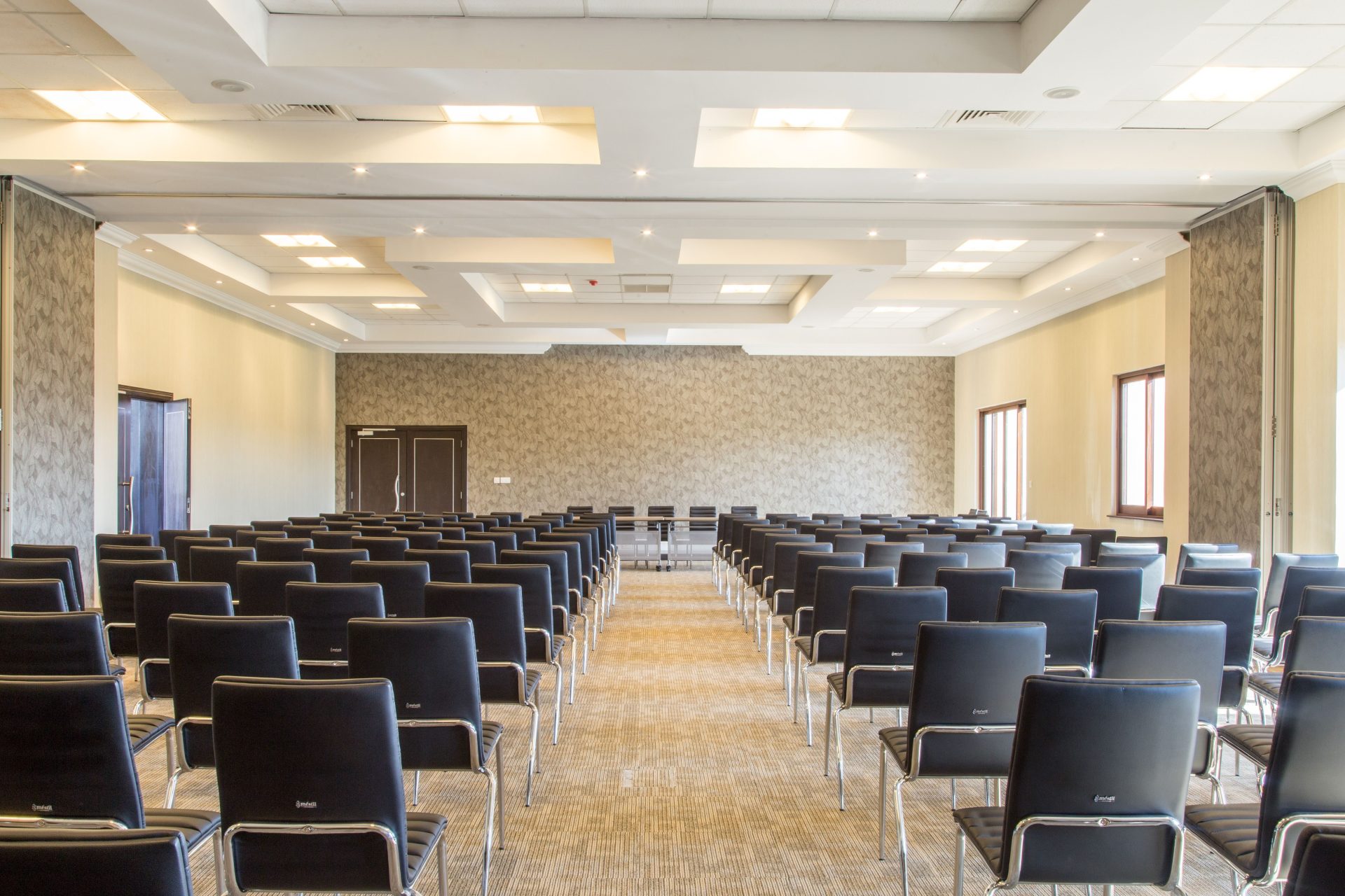 Geräumiger, leerer Konferenzraum mit modernem Design und ordentlich angeordneten schwarzen Stühlen.