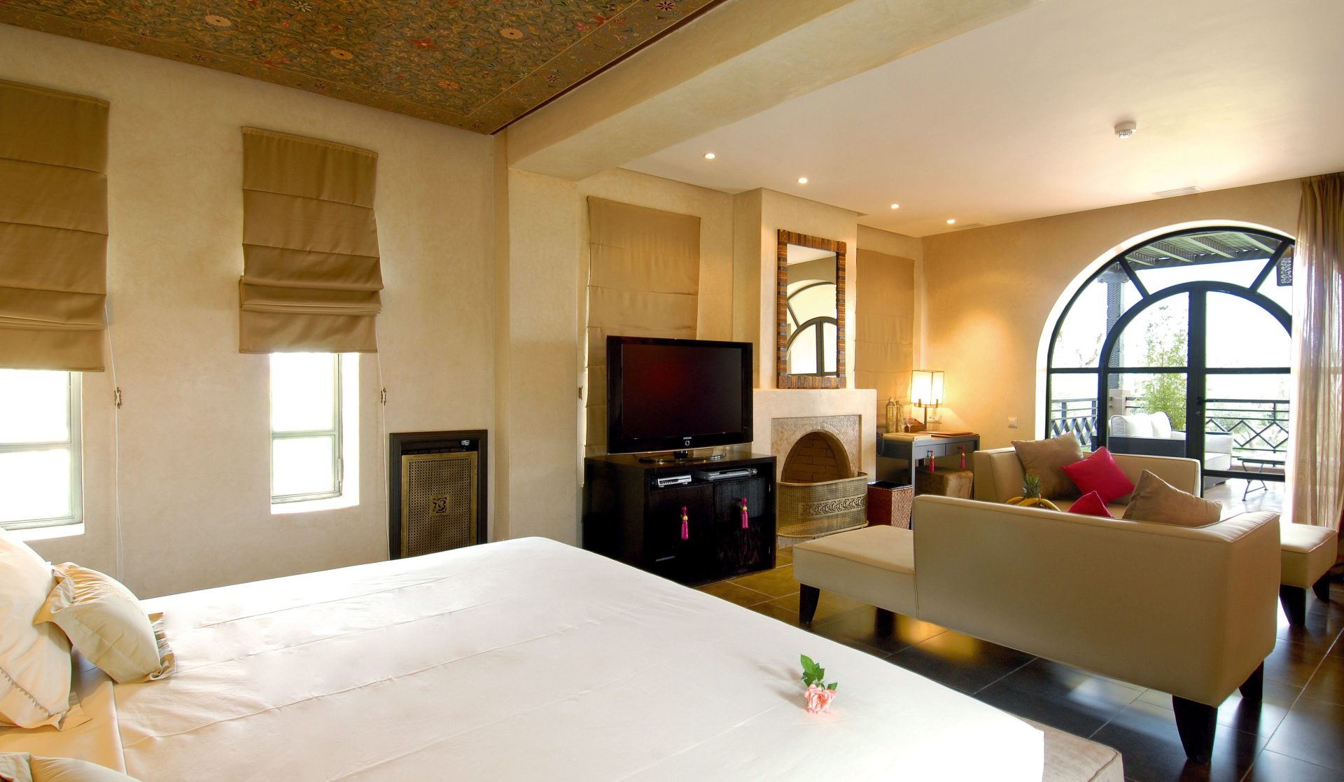 Elegantes, modernes Schlafzimmer-Ensemble mit gemütlicher Sitzecke, großen Fenstern, TV und Kamin, das Wärme und Luxus ausstrahlt.
