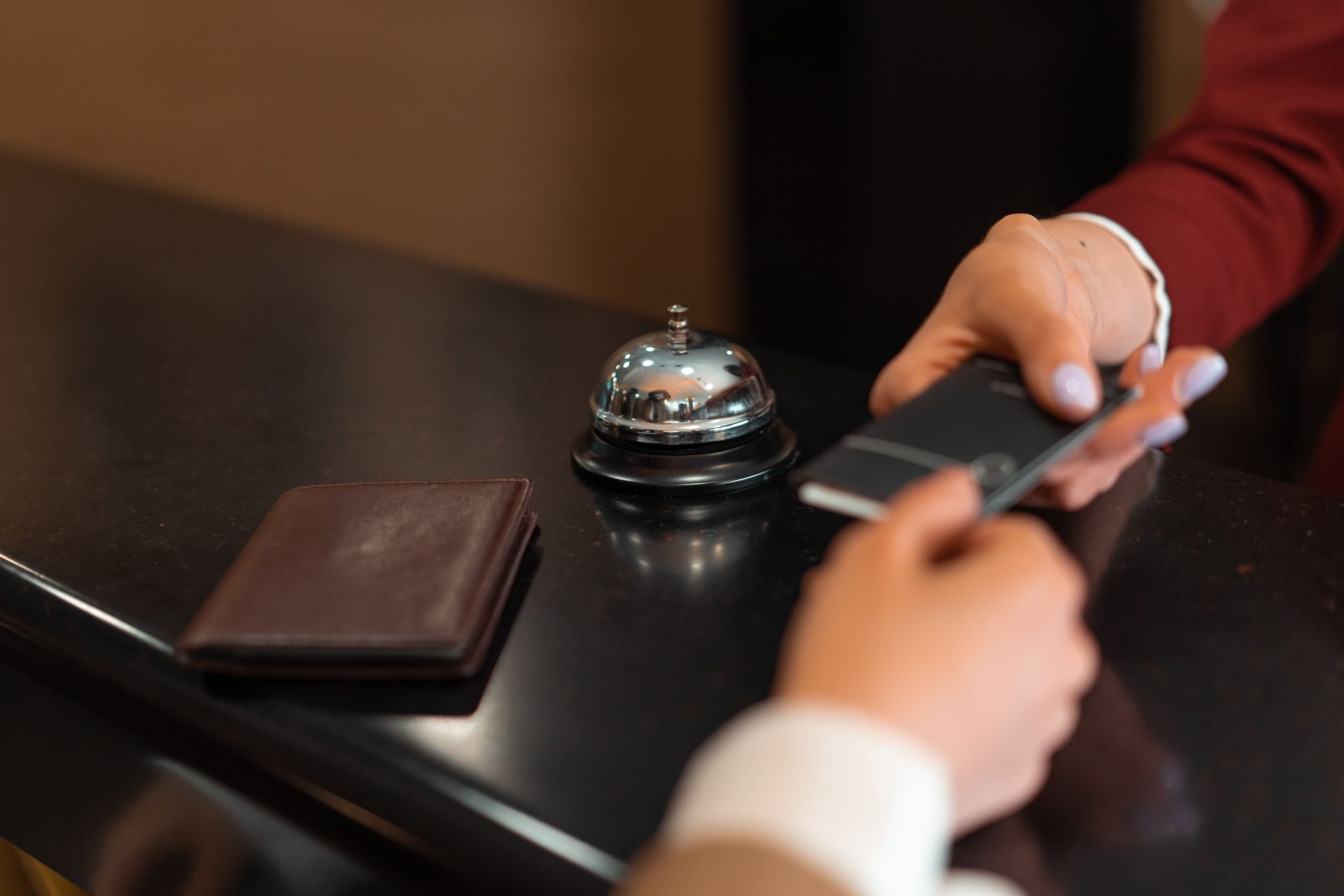 Nahaufnahme eines Hotel-Check-ins mit Smartphone und Kartenzahlung an der Rezeption.